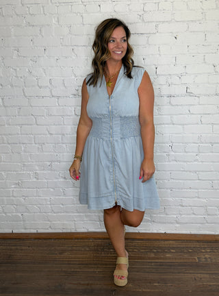 A woman wearing a light blue sleeveless button-front dress with a smocked waistband.
