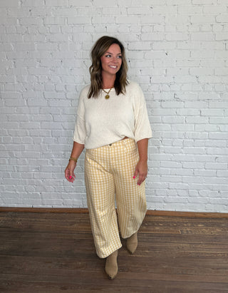 Cream short-sleeve top and yellow-and-white gingham barrel pants, paired with tan ankle boots.