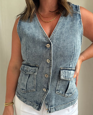 Woman wearing a denim vest over a white top against a neutral background