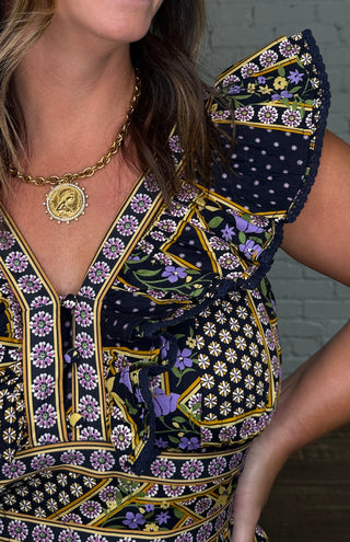 Close up view of a short sleeve midi dress with pockets featuring a navy, purple, orange, green and yellow geometric pattern.