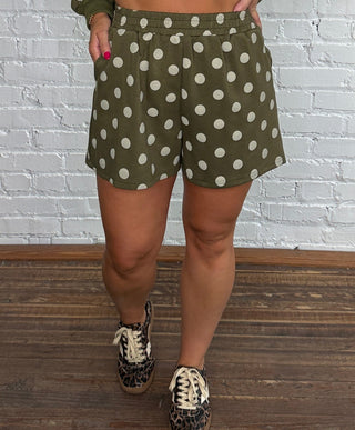 A woman modeling a matching olive green and white polka dot lounge set.