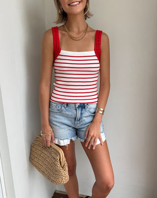 Woman wearing a red and white striped tank top and denim shorts, standing indoors.