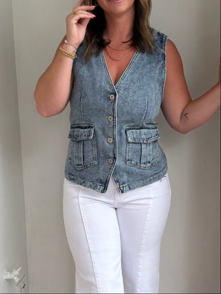 Woman standing in a doorway wearing a denim vest and white pants.