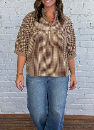 Women wearing a gingham tan and brown v-neck top paired with denim and boots