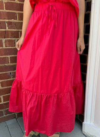 Person wearing a red skirt standing on a porch with a brick wall background