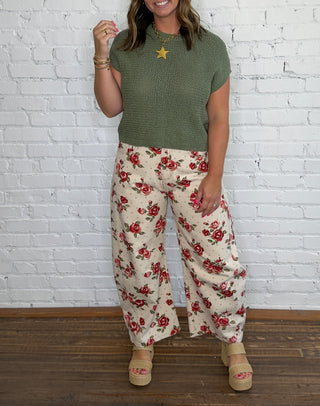 A woman modeling a short-sleeve olive green knit top and cream wide-leg pants with a red floral pattern.