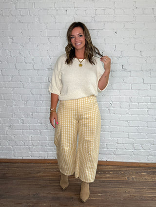 Cream knit short-sleeve top and yellow-and-white gingham barrel jeans with tan ankle boots.