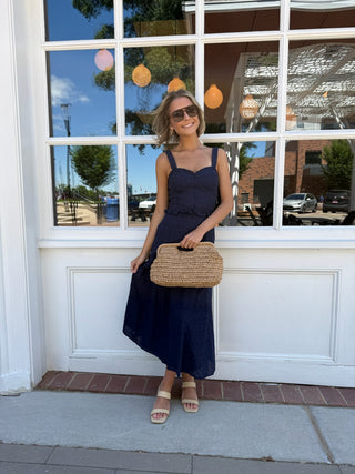 Woman in a navy matching set holding a straw bag in front of a store window.
