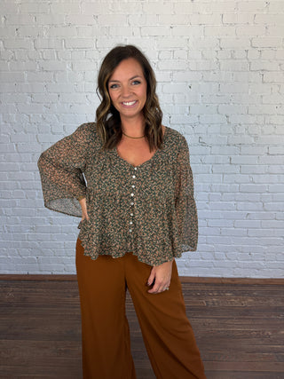 Women wearing brown pants paired with a teal and brown floral flowy top and boots.
