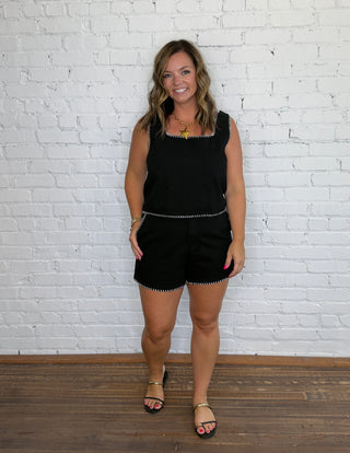 A woman modeling a black sleeveless matching set with decorative white trim.