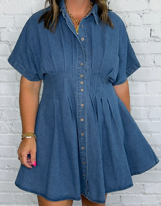 A woman wearing a short-sleeve blue denim button-down dress with a flared skirt.