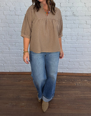 Women wearing a gingham tan and brown v-neck top paired with denim and boots