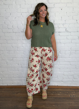 A woman modeling a short-sleeve olive green knit top and cream wide-leg pants with a red floral print.