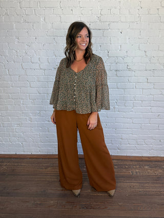 Women wearing brown pants paired with a teal and brown floral flowy top and boots.