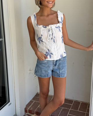 Woman standing in a doorway wearing a floral top and denim shorts.