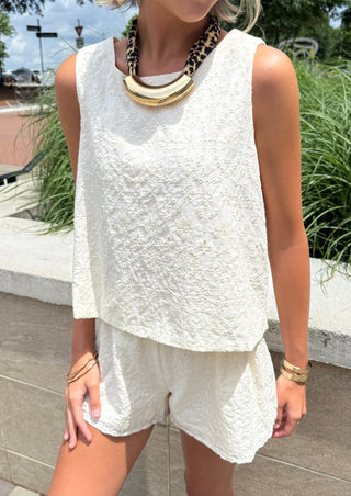 Woman wearing a cream sleeveless top with matching shorts and a leopard print necklace.