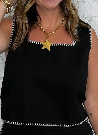 A woman wearing a black sleeveless matching set with white contrast stitching.