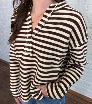 Person wearing a striped shirt with a hood, lying on a white textured surface.