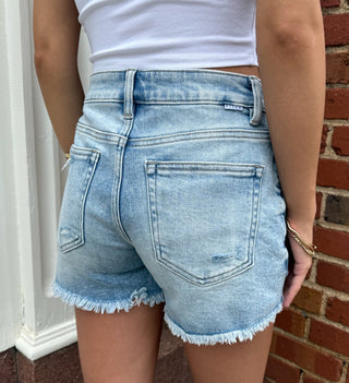 Women wearing light blue denim shorts and a white crop top against a brick wall.
