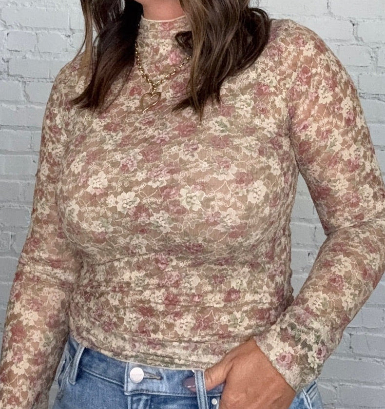 Person wearing a floral long-sleeve top and blue jeans against a brick wall.