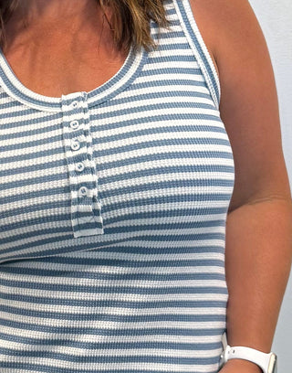 Woman wearing a blue and white striped tank top and white pants.