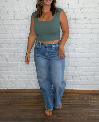 A woman modeling a sage green scoop-neck crop top and light-wash blue jeans.
