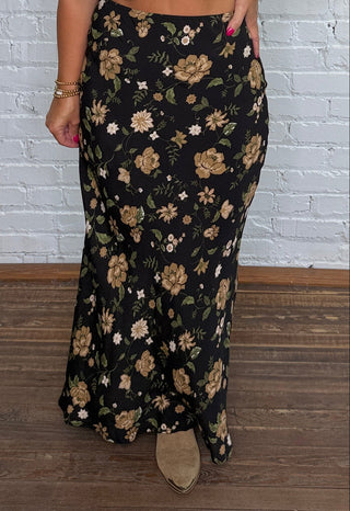 A woman wearing a black maxi skirt with a beige floral pattern.