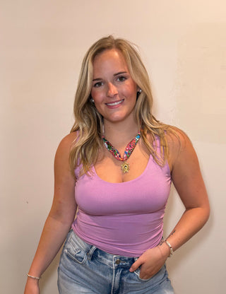 Woman wearing a purple tank top and denim shorts standing against a white wall.