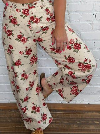 A person wearing wide-leg cream pants with a red rose floral print.