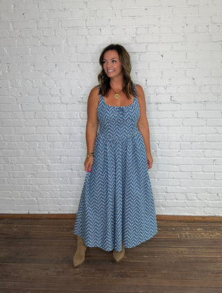 Sleeveless blue and white embroidered chevron-patterned maxi dress and tan boots.