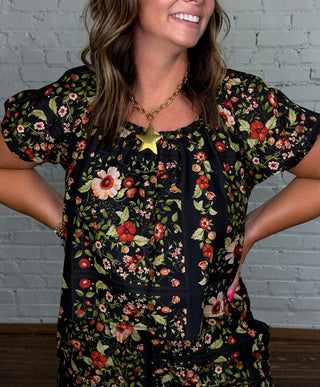 A woman wearing a black short-sleeve floral matching set with red and green floral print.