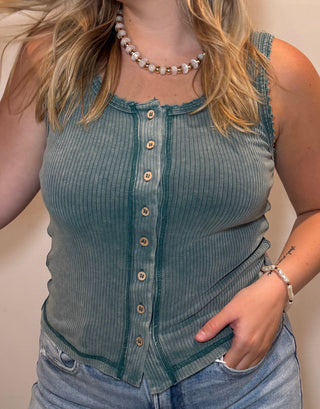 Woman wearing a green sleeveless top and denim shorts indoors.