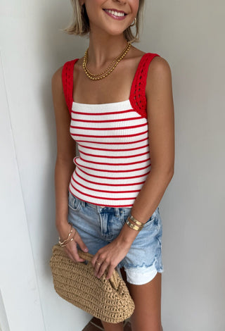 Woman wearing a red and white striped tank top with denim shorts, holding a straw clutch.