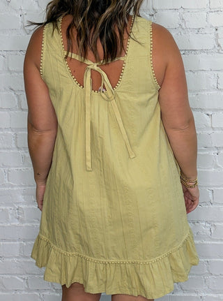 A woman wearing a sleeveless light yellow-green linen dress, viewed from the back.