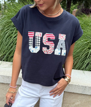 Woman wearing a navy blue t-shirt with 'USA' block print and white pants.