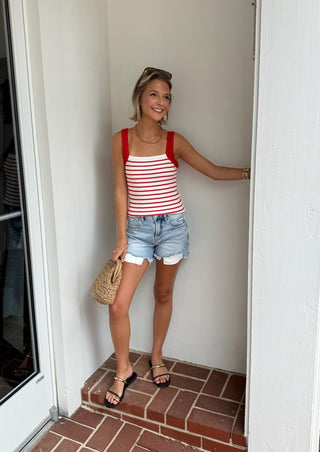 Woman in a red and white striped tank top and denim shorts standing in a doorway.