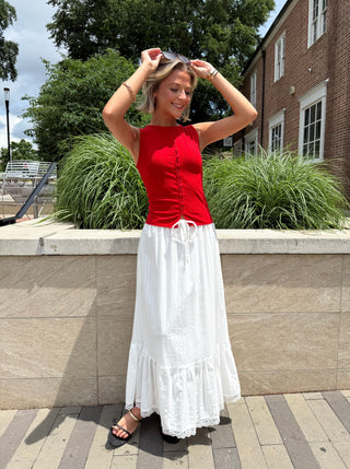 Woman in a red top and white skirt standing outdoors near a building