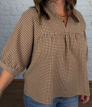 Women wearing a gingham tan and brown v-neck top paired with denim and boots