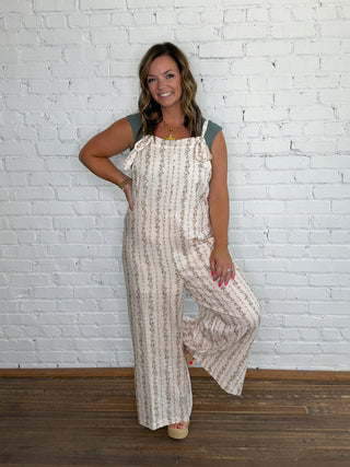 A woman modeling a sleeveless cream jumpsuit with a vertical brown floral pattern.