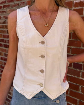 Person wearing a white denim vest and blue jeans against a brick wall.