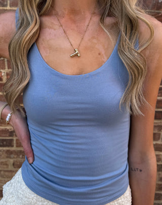 Woman wearing a blue tank top and beige skirt against a brick wall.