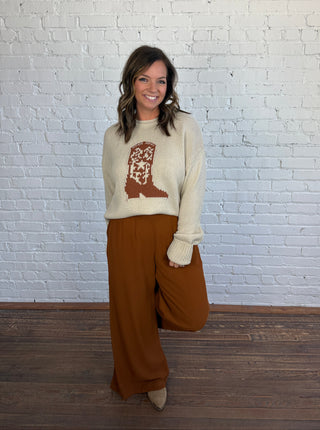 Women wearing brown trousers with a cream tsweater and cowboy boot graphic. 