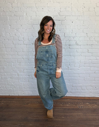 Woman wearing barrel overalls, paired with a burgundy and blush striped top and brown shoes.