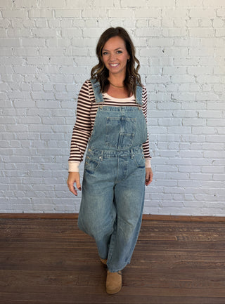 Woman wearing barrel overalls, paired with a burgundy and blush striped top and brown shoes.