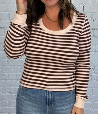 Women wearing a blush and burgundy striped top with jeans and brown shoes.