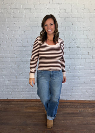 Women wearing blush and burgundy striped top with jeans and brown shoes.