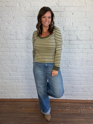 Woman wearing an olive and sage green striped top paired with medium washed denim jeans, and taupe boots.