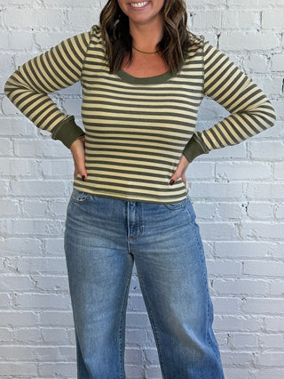 Woman wearing an olive and sage green striped top paired with medium washed denim jeans, and taupe boots.