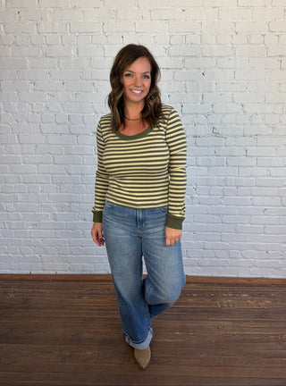 Woman wearing an olive and sage green striped top paired with medium washed denim jeans, and taupe boots.