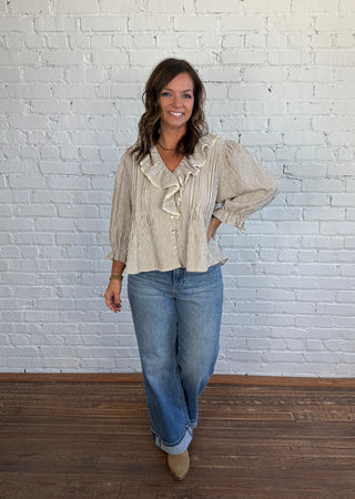Woman wearing a brown and cream striped top with a V-neck collar and lace detail with jeans and boots.